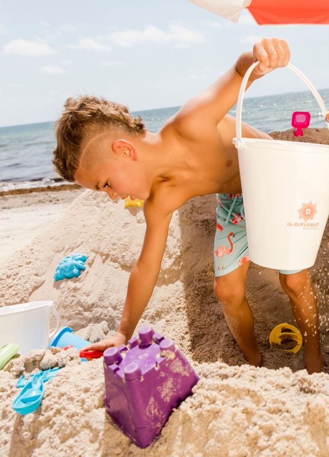 Kids on beach with pale and spade and kid bending