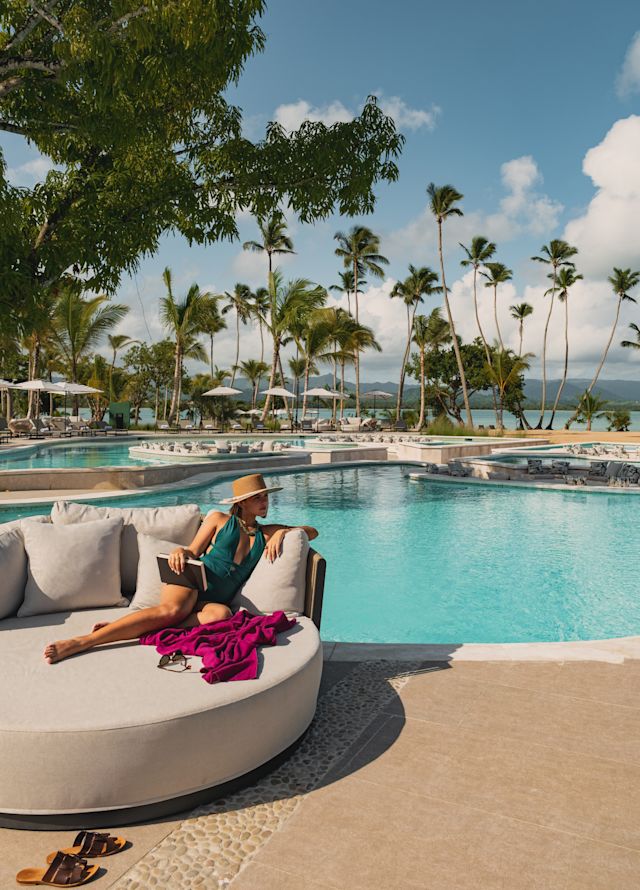 A woman sitting in a soft full lounge chair at the main pool.