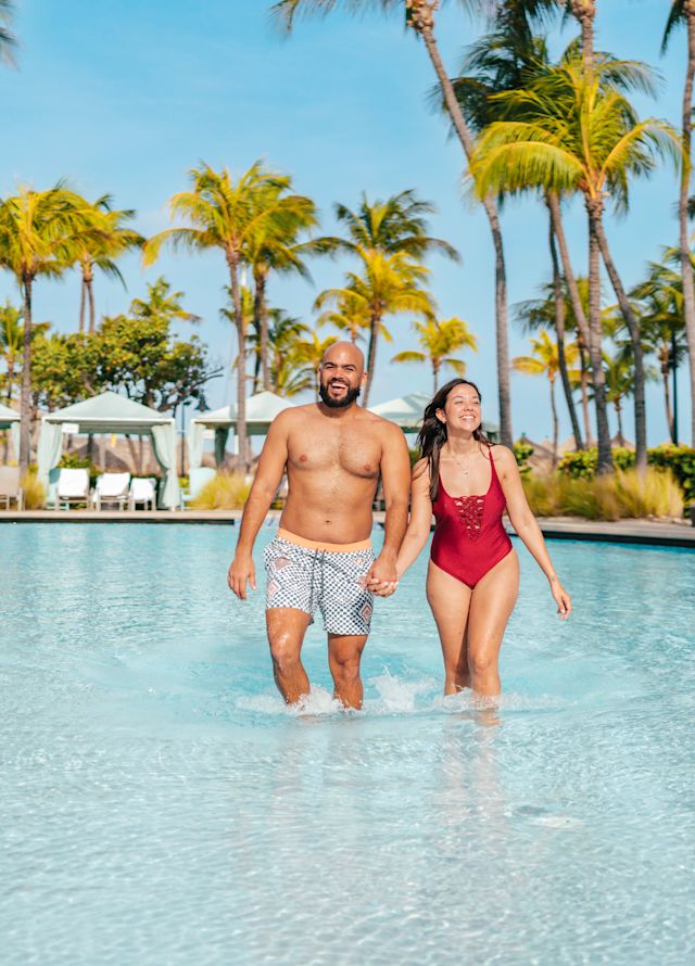 couple in a swimming pool area with palm trees and lounge chairs