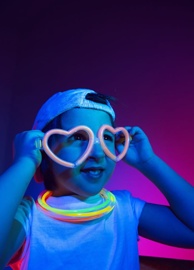 Kleines Kind mit großen herzförmigen Gläsern und leuchtenden Strohhalmen am Nacken