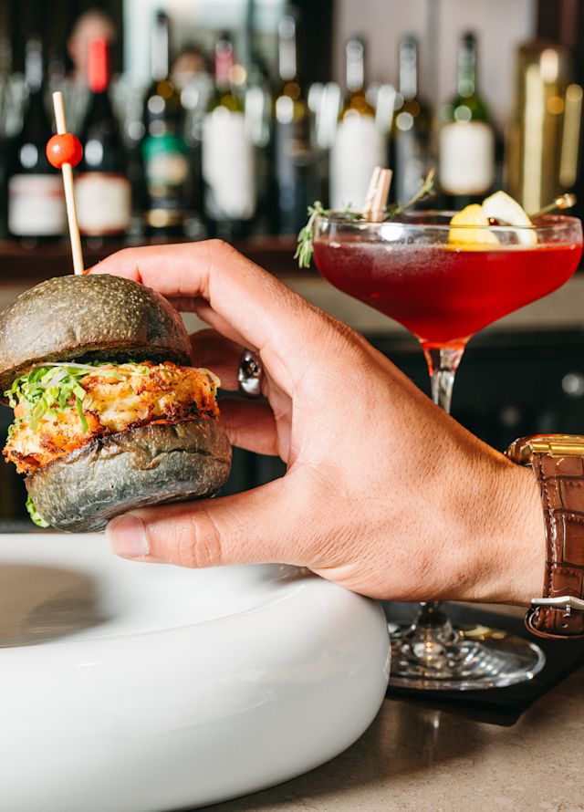 A Man's Hand Holding a Slider at the Bar of SER Steak and Spirits Restaurant