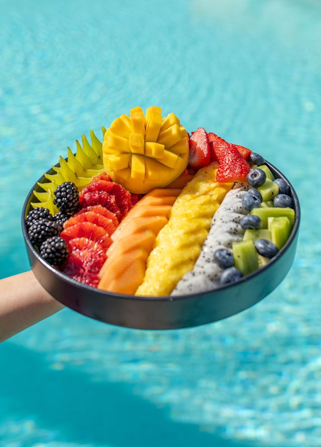 Neatly sliced tropical fruits in a bowl, hovering over a bright blue pool.