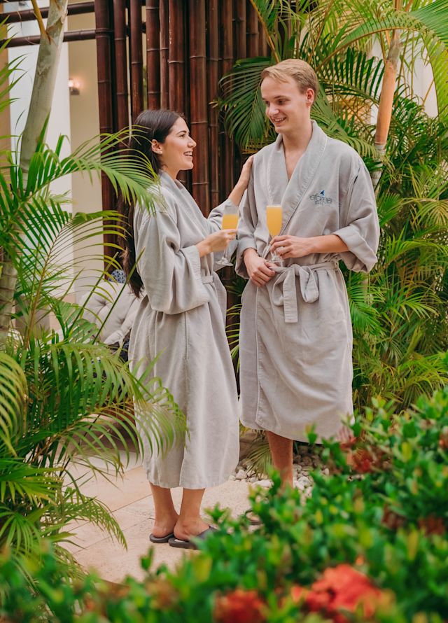 Couple in robes enjoying a drink surrounded by tropical trees