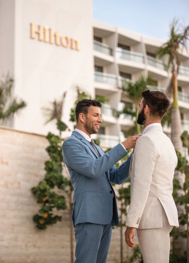 One man fixes another mans tie in front of a Hilton hotel
