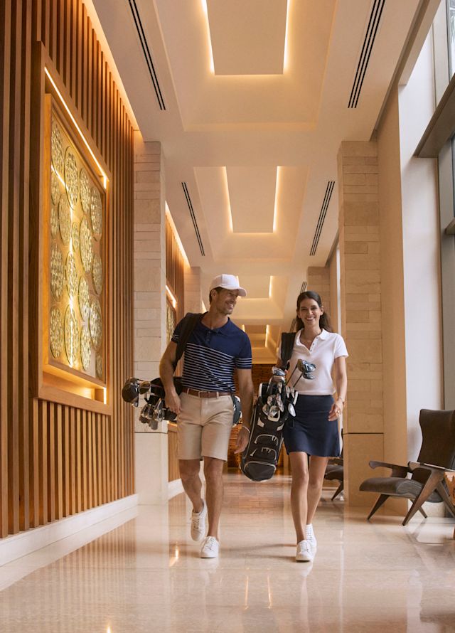 Woman and man walking down a hotel corridor with golf clubs