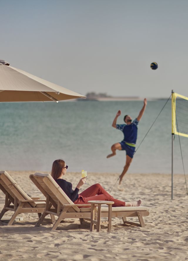 People playing volleyball on beach while woman watches