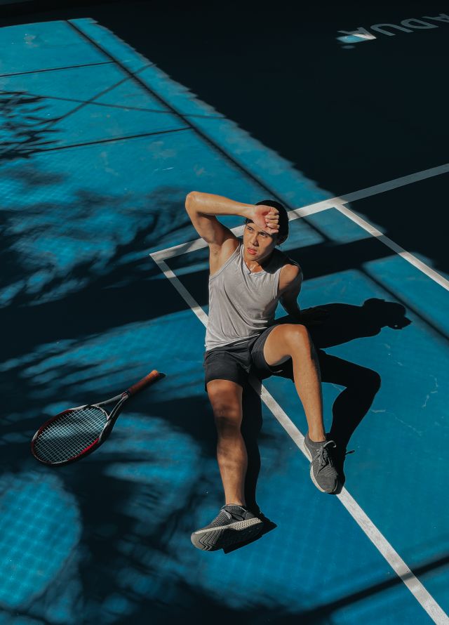 Mann liegt auf einem Tennisplatz mit Tennisschläger neben ihm