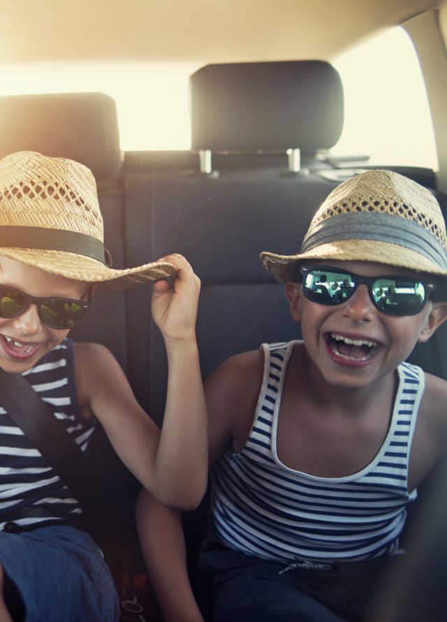 Niños con anteojos de sol riendo en la parte posterior de un automóvil