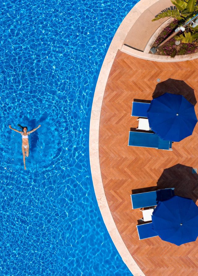 Donna che nuota in un'ampia piscina esterna con salotto sotto gli ombrelloni