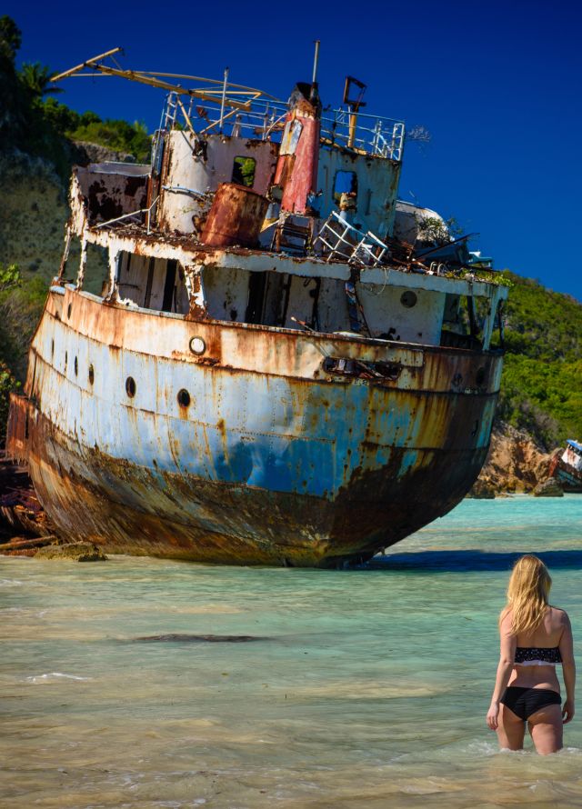 Woman wading in ocean with shipwreck in front of her