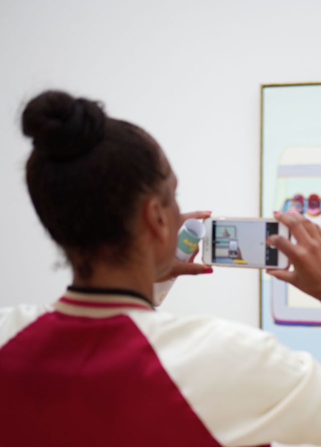 Two women taking photos on phones of art on a wall