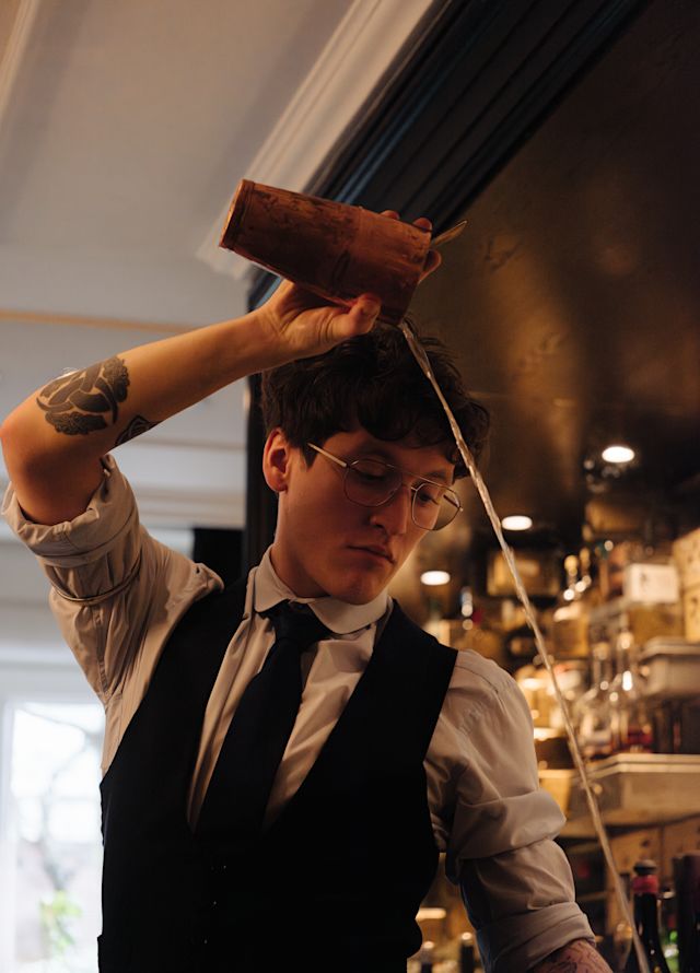 A male bartender doing a high pour for an avant-garde cocktails available at Vault Bar.