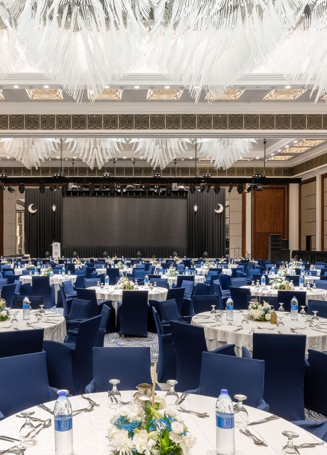 Al Joud Ballroom setup with white covered round tables and blue covered seats