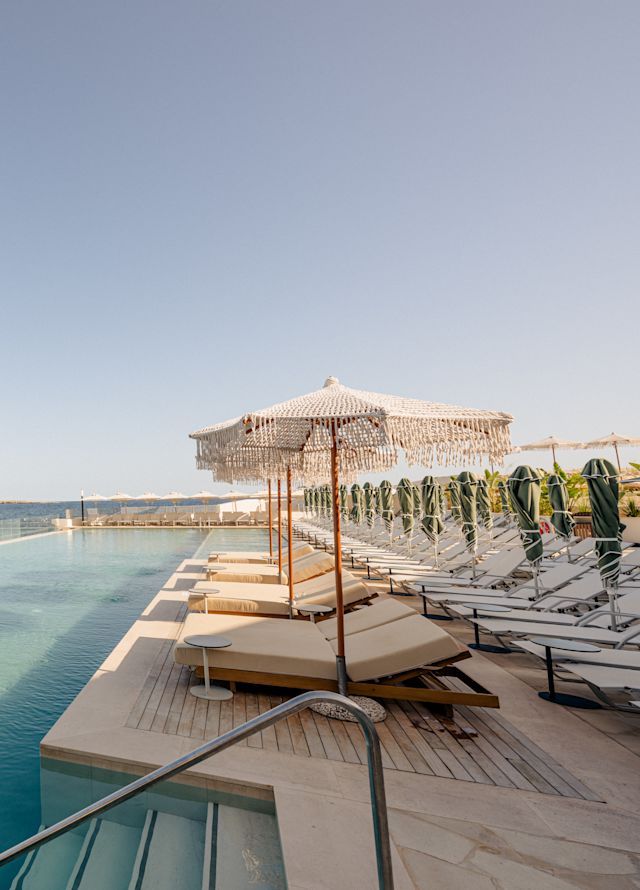 Área do pátio com espreguiçadeiras com vista para a piscina e o mar em um dia ensolarado