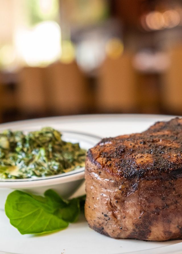 Filet Steak on a plate with a bowl of greens