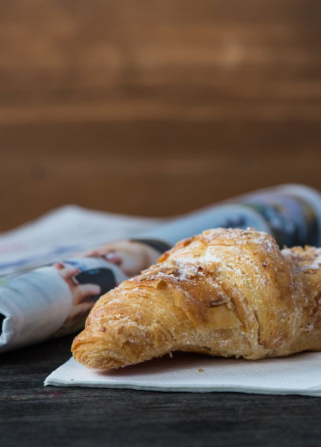 Take away coffee and fresh croissant and newspaper on wooden background