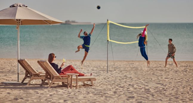 People playing volleyball on beach while woman watches