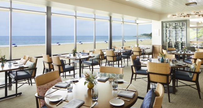 restaurant seating area with round tables and view of beach through windows