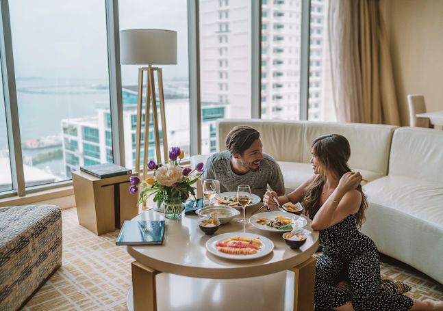 Man and Woman Talking over Dinner at a Coffee Table Near Large Windows