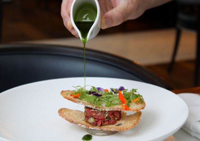 a person adding sauce to a plate of food at The Coburg Restaurant