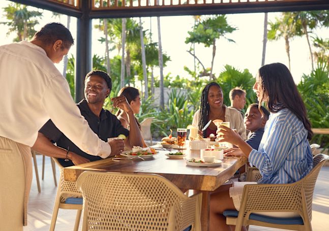 Man, two women and a boy are enjoying dinner on the restaurant terrace in the evening sun.