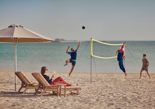 Des personnes jouant au volley-ball sur la plage tandis qu'une femme regarde