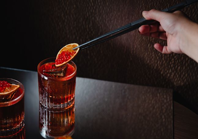 Person Adding an Orange Slice to a Negroni Glass on a Table at Skyline Rooftop Bar