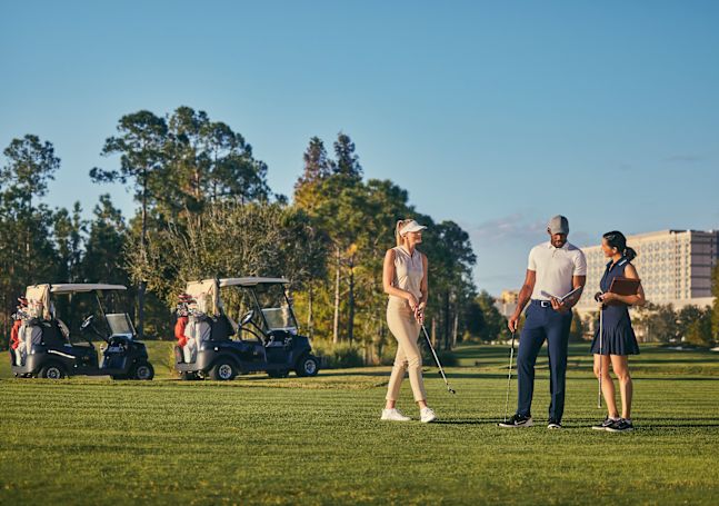 Man and two women standing on golf course with buggies in the background