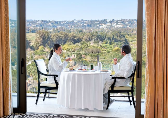 Man and woman in white robes enjoying breakfast on guest room balcony