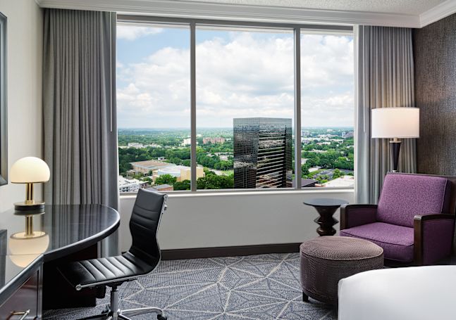 King room city view with edge of bed and view of window and alternative city view with table and purple chair