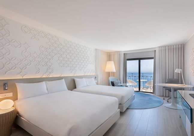 Camera con due letti, scrivania e balcone con vista mare