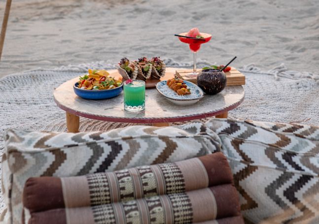 夕暮れ時のビーチの屋外テーブルに盛り付けられたお食事とお飲み物