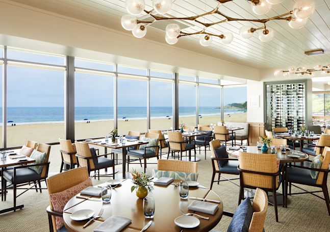 restaurant seating area with round tables and view of beach through windows