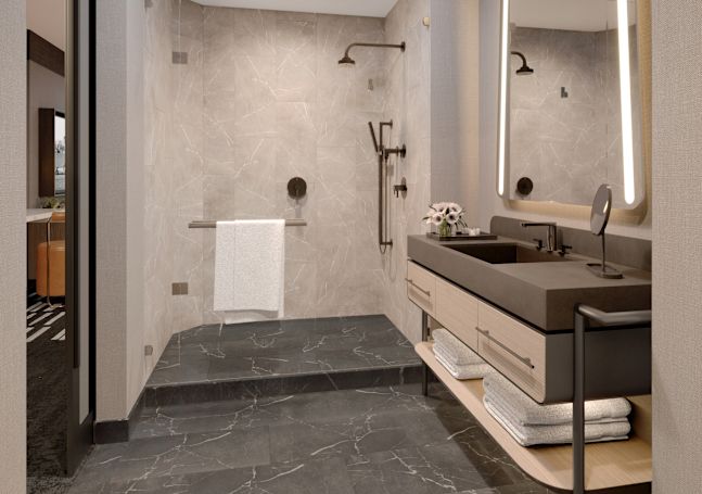 Koupelna pro hosty s bezbariérovou sprchou, jednolůžkem a osvětleným zrcátkem