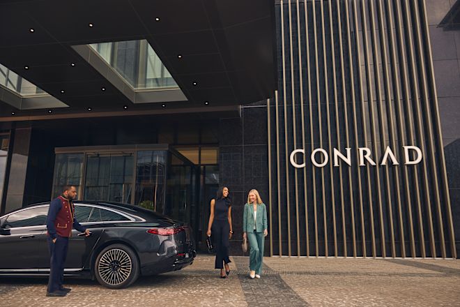 Two women leaving hotel and walking past car in drive