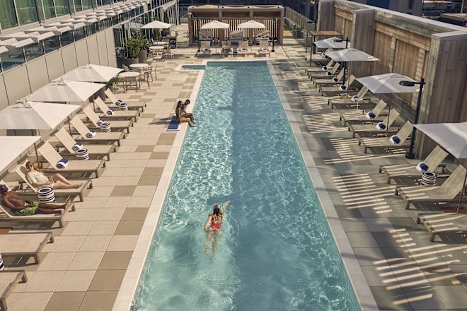 Two woman relax at the side of the pool, while woman in red swimsuit does lengths