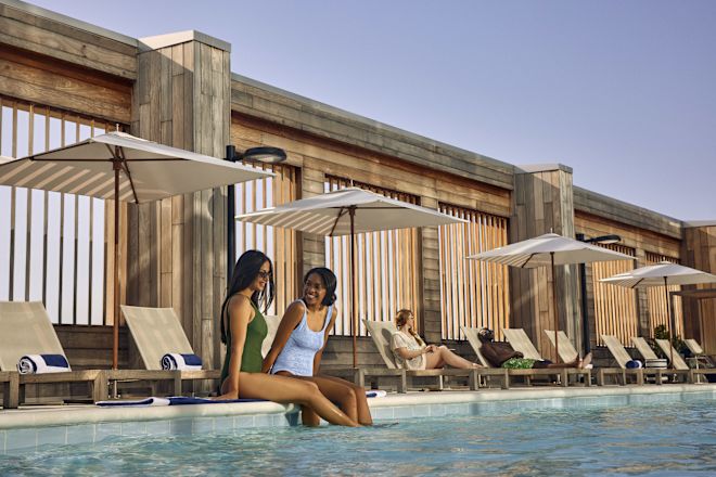 Two woman relaxing by the side of the pool, with legs in the water