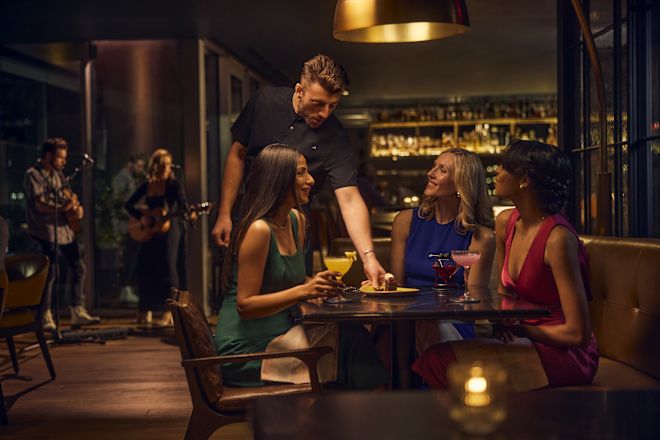 Three women sitting in restaurant area while staff member serves