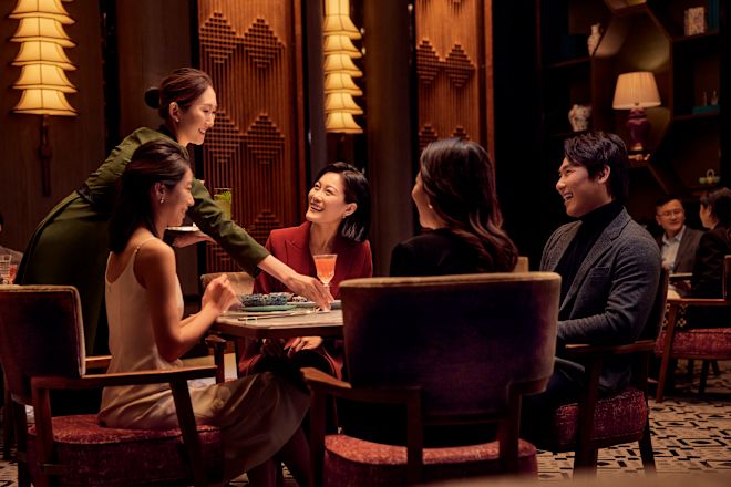 レストランのテーブルに座り、待っているスタッフがテーブルにドリンクを置いたグループ