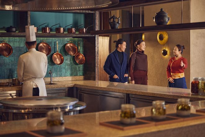 Pria dan wanita berjalan melewati restoran dipandu oleh anggota staf saat koki bekerja