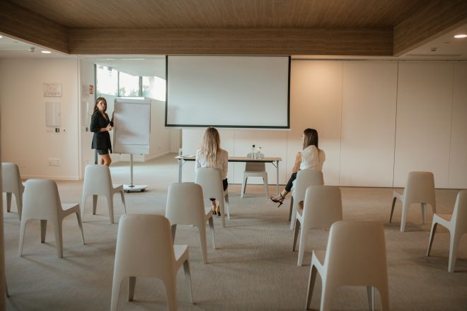 Frauen sitzen im großen Meetingraum mit Projektionsleinwand
