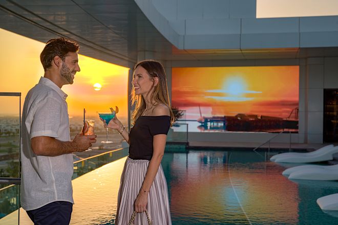 Man and woman with drinks near balcony at sunset