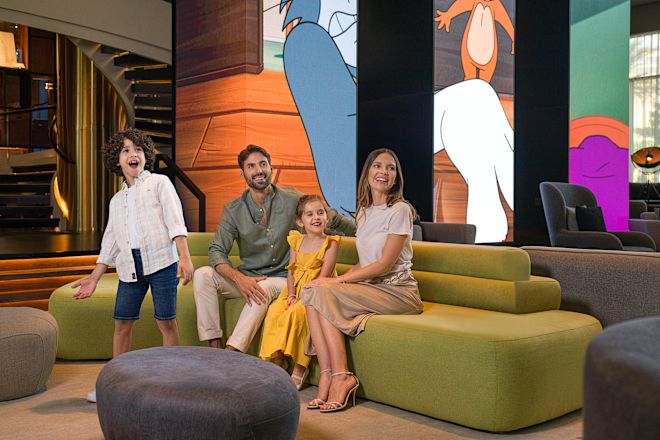 Family on green couch in lobby with Tom and Jerry murals behind them