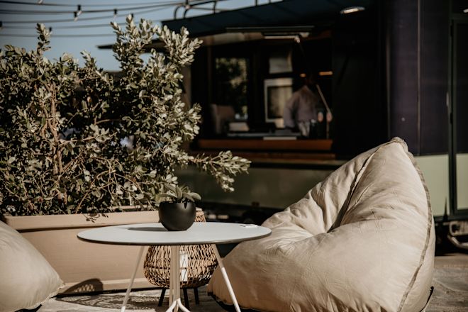 Amphiteatro outdoor seating area with a white table, food truck, beige bean bag chairs, and potted plants.