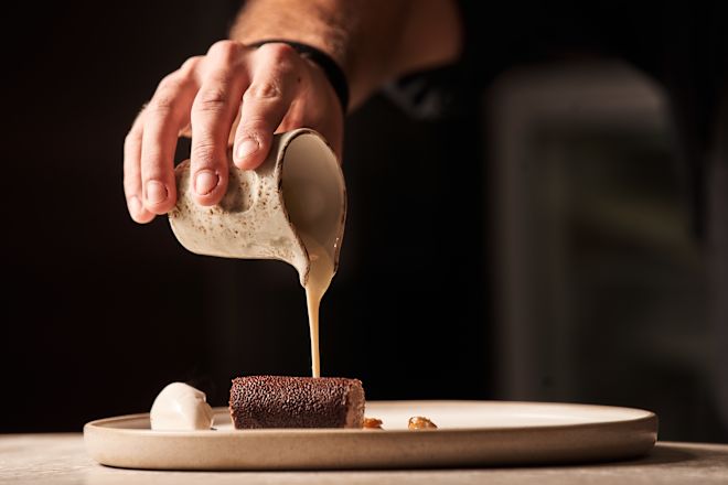 Man Pouring Sauce on a Plate at Cretamos Restaurant