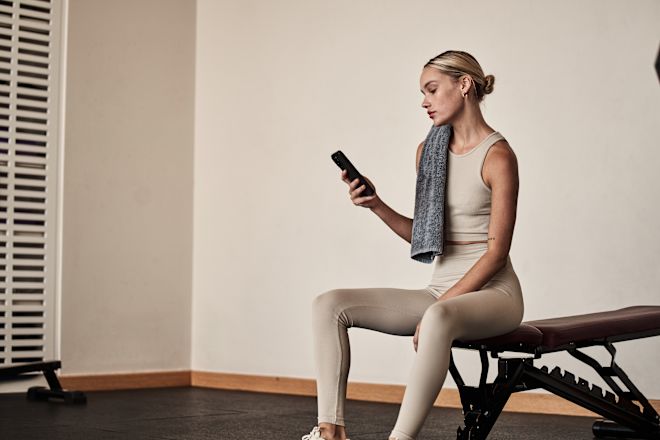 Woman Resting, Looking at Her Cell Phone in Fitness Center