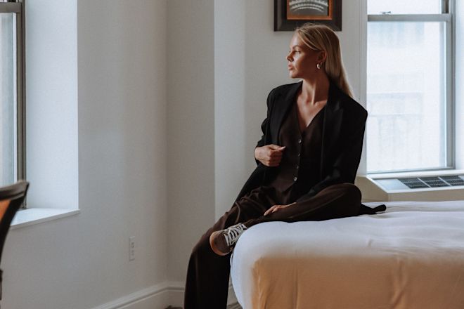 Woman Wearing a Black Suit Sitting on a Bed in a Guest room