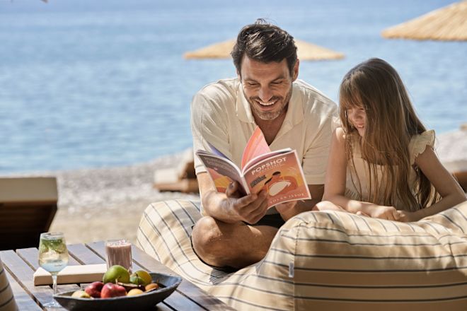 Father and Daughter Reading a Book and Snacking on Fruits at the Beach