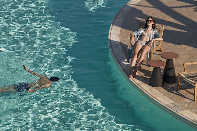 Man Swimming in the Pool and a Woman Getting a Sun Tan Relaxing on a Lounge Chair