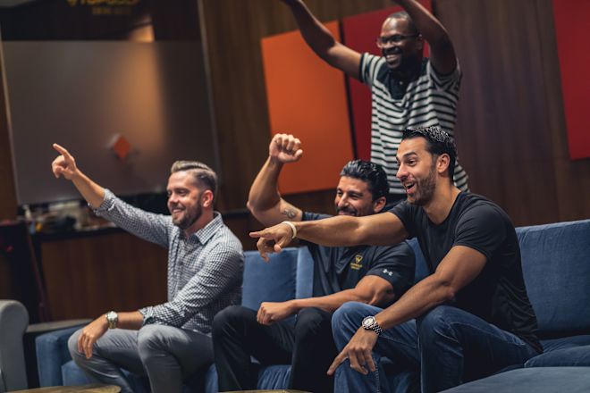 Group of men with their hands in the air. 3 men are seating on a couch and the 4th is standing
